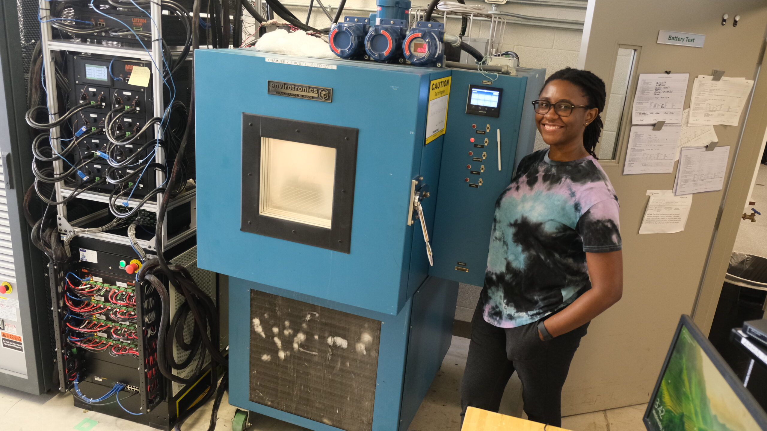 Lucia standing beside the small thermal chamber, which is turned on. Gives a size comparison of the equipment in the lab.