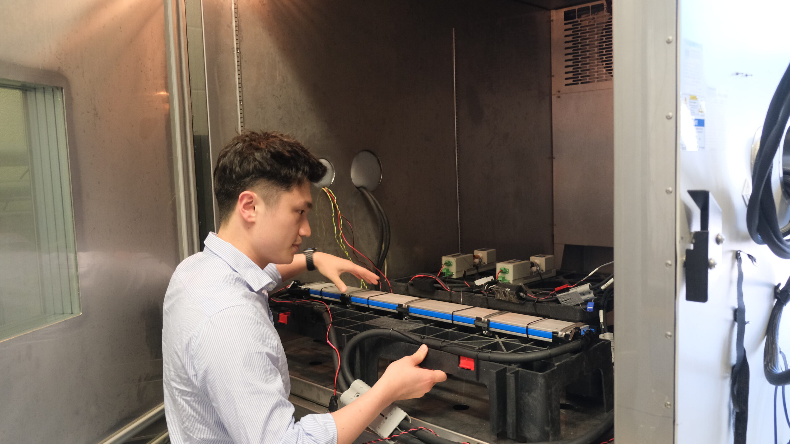 Junran securing a blade cell inside a large chamber, ensuring it is properly positioned for testing. The chamber interior is visible, with various equipment set up.