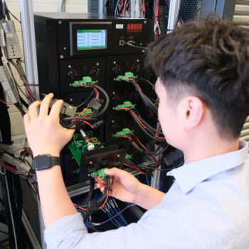 Junran securing battery cells inside a microthermal chamber, with various cables connected to the chamber and an Arbin control unit displaying data on a screen.