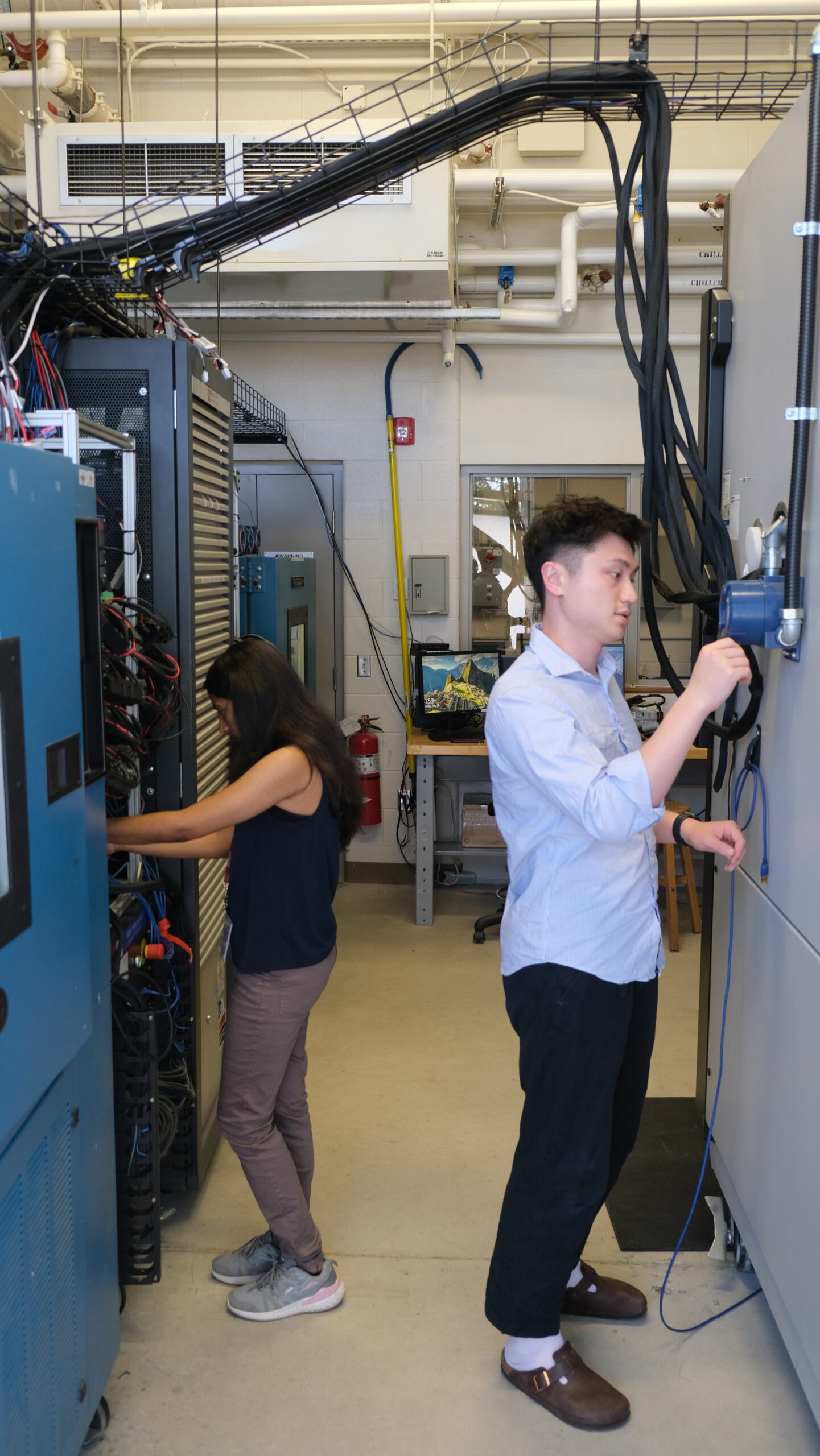 Sobhika working on the 8-channel cycler on the left side, Junran is looking at the large thermal chamber on the right. This image indicates the size of the lab and equipment, compared to the researchers.