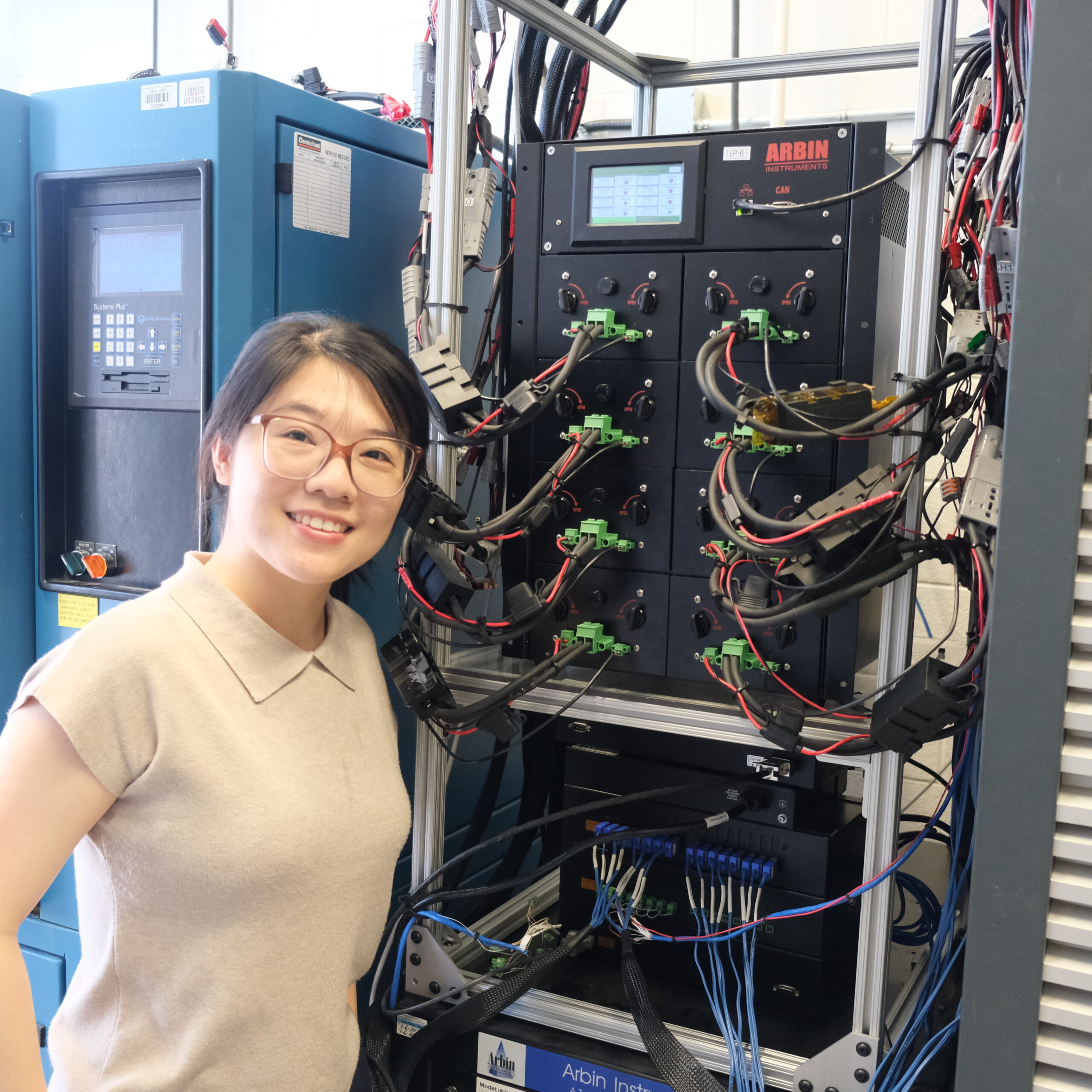 Qi in front of the microthermal chamber to indicate its size, with various cables and connections visible behind her