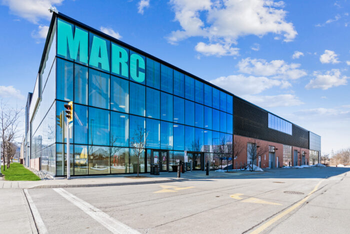 Outside of the McMaster Automotive Resource Centre (MARC) building with large glass windows and the MARC logo in the front, highlighting the facility.