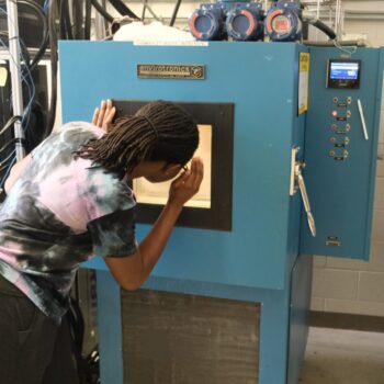 Lucia looking into a blue chamber with the light turned on, checking to verify the secure connections inside. The chamber features control buttons and a small display on the right side.