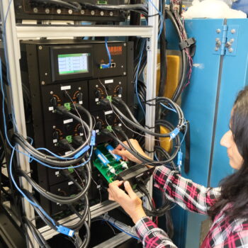 Sobhika placing her battery cells inside a chamber for temperature testing, with various cables connected to the chamber and an Arbin control unit displaying data on a screen