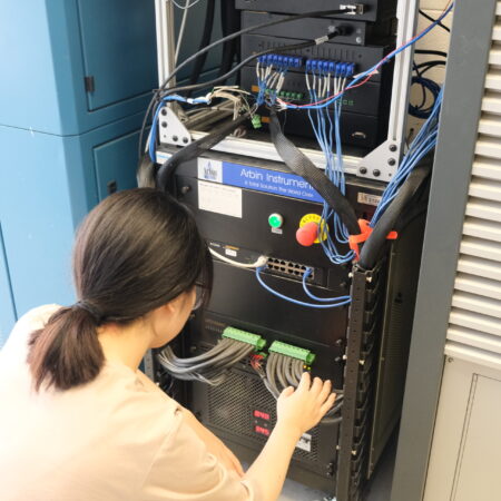 Post-doctoral researcher Qi setting up connections on the Arbin 8-channel battery cycler, adjusting cables and connectors in a laboratory setting.