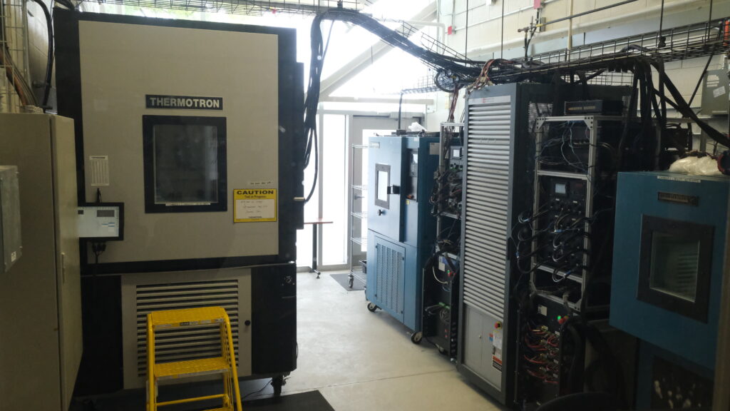 Interior of a cell testing lab featuring four thermal chambers and various cell testing equipment. The lab is filled with machinery, including a large unit labeled 'Thermotron' and other specialized testing devices.