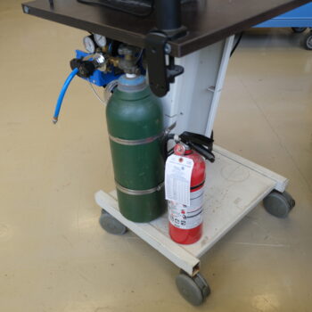 Tanks located under the trolley cart that holds the welder. The left tank contains argon gas, and the right is a fire extinguisher.