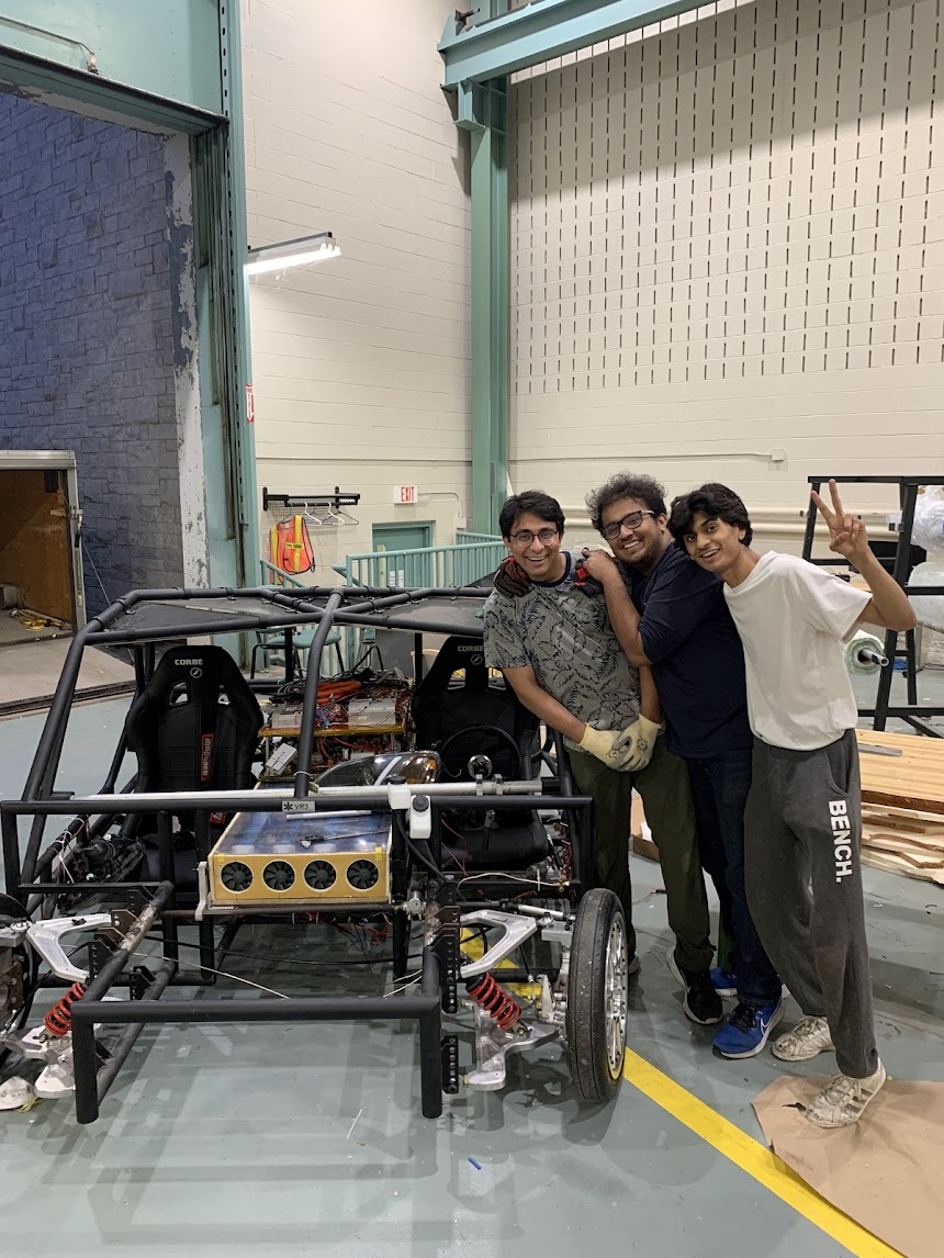 From left to right, electrical sub-team lead Kavish, suspension and vehicle dynamics sub-team lead Anand, and Aeroshell sub-team lead Aryan. Smiling and standing beside the mechanical frame of the final iteration of the vehicle, Origin.