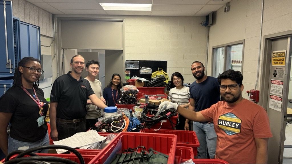 The team looking happy during a lab cleanup day. From left to right, Lucia, Dr. Kollmeyer, Junran, Sobhika, Qi, Romulo and Biswanath. There are items being organized inside red boxes which are on the table in the middle of the room