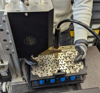 A student wearing safety gloves using a parallel weld head attachment to make precise welds on a battery module. The module is held securely under the welding attachment to ensure exact placement.